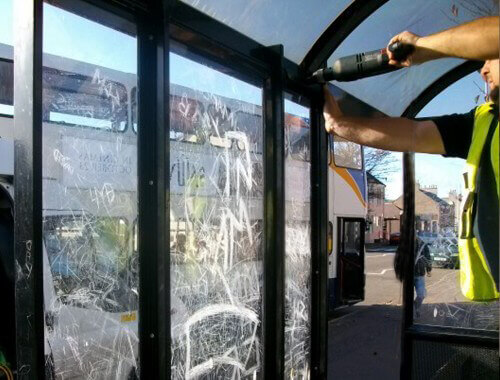 view of a Trueform employee replacing damaged glazed screens on a bus shelter.