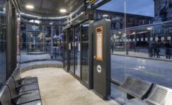 Modern bus shelter infrastructure with seating, lighting, and wayfinding signage, showing passengers using a well-designed urban transport waiting environment.
